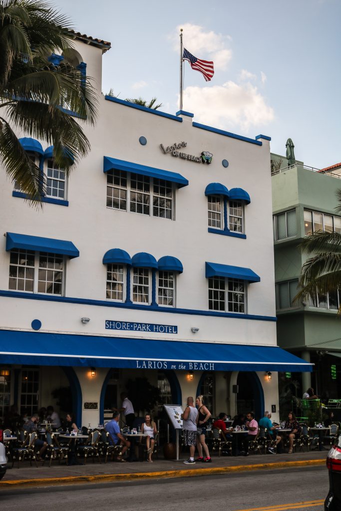 Fotografia mostra hotel em South Beach - Miami Beach, com restaurante cheio de pessoas na calçada.